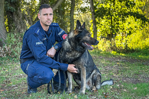 Zdjęcie przedstawia kucającego policjanta obok jego psa