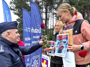 Na zdjęciu policjant wręcza uczestniczce biegu różę.
