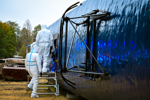 Zdjęcie przedstawia policjantów w kombinezonach ochronnych wchodzących do wraku wagonu.