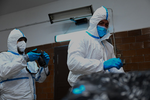 zdjęcie przedstawia policjantów w ochronnych kombinezonach w trakcie oględzin manekina imitującego ofiarę katastrofy.