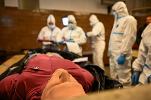 zdjęcie przedstawia policjantów w ochronnych kombinezonach w trakcie oględzin manekina imitującego ofiarę katastrofy.