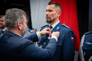 mężczyzna przypina do munduru medal nagrodzonemu policjantowi