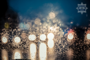 szyba, na którą pada deszcz i widoczne z oddali światła