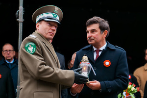 generał Straży Granicznej trzymający zapalony znicz obok cywila