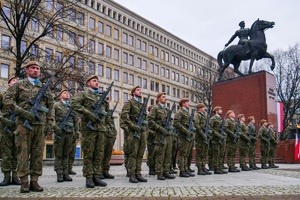 żołnierze z bronią palną na tle pomnika