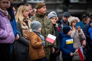 żołnierz oraz cywile, z których niektórzy trzymają flagi