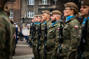 polscy żołnierze trzymający broń palną na tle budynku