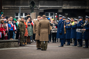 żołnierz składa meldunek drugiemu żołnierzowi na tle policyjnej orkiestry