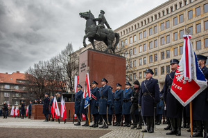policjanci ze sztandarem obok pomnika Piłsudskiego i flagi RP