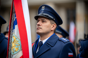 policjant obok sztandaru oraz flagi RP