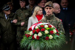 żołnierz trzymający w ręku wieniec biało-czerwonych kwiatów