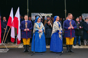 osoby ubrane w stroje ludowe przy fladze Polski