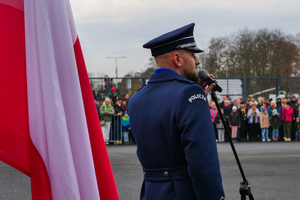 policjant przemawia przez mikrofon przy fladze Polski