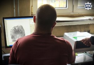 mężczyzna siedzący przy komputerze, na monitorze którego wyświetlony jest odcisk palca