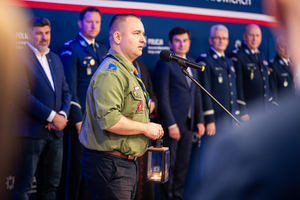 zdjęcie przedstawia przedstawiciela harcerstwa przy mikrofonie, w tle policjanci i uczestnicy uroczystości.