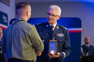 zdjęcie przedstawia komendanta ściskającego rękę mężczyzny reprezentującego harcerstwo, a drugiej ręce trzymającego symboliczny lampion.