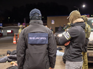 zdjęcie przedstawia trzech funkcjonariuszy odwróconych plecami, jeden z nich posiada bluzę z napisem "Europol", drugi natomiast opaskę z napisem "Policja".