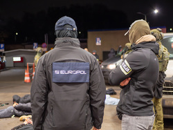 zdjęcie przedstawia trzech funkcjonariuszy odwróconych plecami, jeden z nich posiada bluzę z napisem "Europol", drugi natomiast opaskę z napisem "Policja".