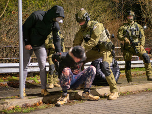 zdjęcie przedstawia funkcjonariuszy Policji oraz Straży Granicznej i mężczyznę, który siedzi na krawężniku.