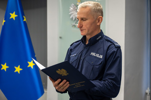 Policjant odczytujący treść dokumentu na tle flagi Unii Europejskiej.