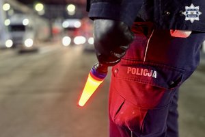 Zdjęcie przedstawia policyjną latarkę oraz policjanta podczas wykonywania czynności kontrolnych