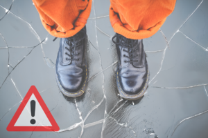 Zbliżenie na czarne buty osoby stojącej na pękającym lodzie.