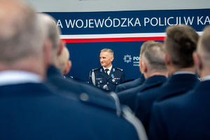 Na zdjęciu widoczny policjant stojący przed innymi funkcjonariuszami