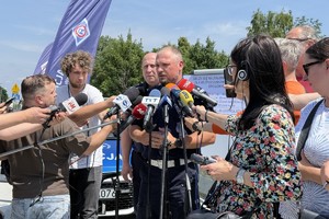 Policjant stojący przed reporterami wypowiada się do mikrofonów.