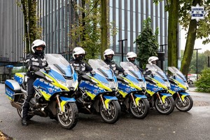 Pięciu policjantów na motocyklach ustawionych w szeregu przed budynkiem.