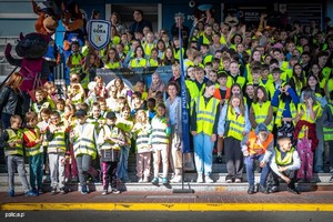 Grupa dzieci i młodzieży w kamizelkach odblaskowych na schodach przed budynkiem.