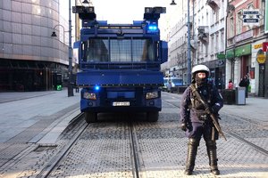 na zdjęciu umundurowany policjant z długą bronią stoi przed pojazdem policyjnym.