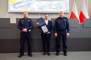 Na zdjęciu widoczni dwaj umundurowani policjanci pomiędzy którymi stoi mężczyzna. Mężczyzna trzyma pamiątkową tabliczkę.