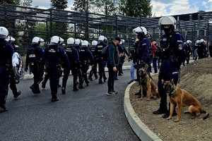 na zdjęciu dwóch umundurowanych policjantów z psami przygląda się grupie maszerujących umundurowanych policjantów