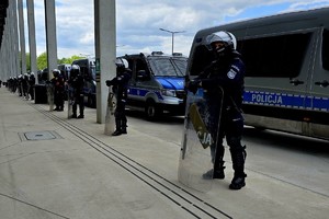 na zdjęciu umundurowani policjanci z tarczami stoją odwróceni tyłem do radiowozów.