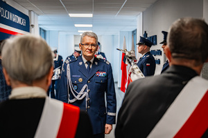 Policjant ubrany w mundur galowy idzie przez korytarz w kierunku pocztu sztandarowego.