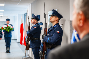 Policjanci stojący przed tablicą upamiętniającą postać insp. dr Adama Kocura z bronią w rękach.