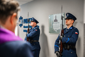 Policjanci pełniący wartę honorową przed tablicą upamiętniającą postać insp. dr Adama Kocura w towarzystwie księdza.