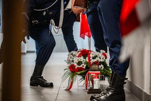 Zbliżenie na policjanta pochylającego się nad wieńcem z kwiatów.