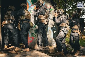 na zdjęciu grupa umundurowanych policjantów wchodzi do ciemnego pomieszczenia