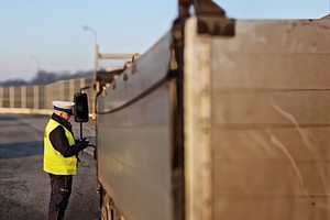 Policjant z urządzeniem do badania stanu trzeźwości stoi  obok samochodu ciężarowego.