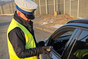 Policjant odczytuje wynik z urządzenia do badania stanu trzeźwości przy opuszczonej szybie samochodu.