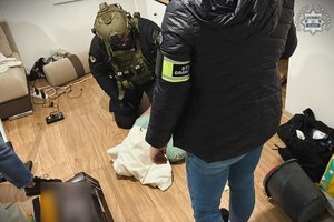 Na zdjęciu widać policjantów, w tym jednego ubranego w specjalistyczną zieloną kamizelkę i kask ochronny.