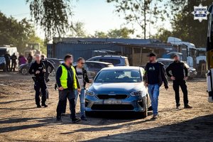 Na zdjęciu widać policjantów umundurowanych i kryminalnych, a w tle baza transportowa i samochody ciężarowe.