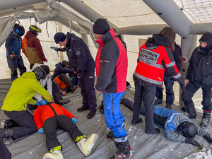 Pod namiotem grupa osób stoi nad leżącymi na ziemi osobami.