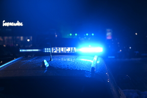 Zdjęcie przedstawia radiowóz policyjny z włączonymi światłami uprzywilejowania koloru niebieskiego w nocy