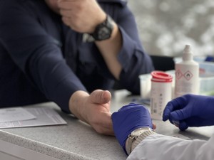 Zbliżenie na dłonie policjanta i osobę pobierając krew w niebieskich rękawiczkach.