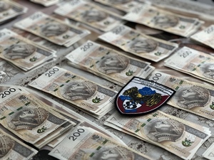 Zbliżenie na rozłożone banknoty i emblemat Wydziału do spraw Zwalczania Przestępczości Pseudokibiców