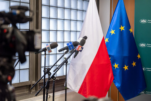Grafika przedstawia flagi Polski i Unii Europejskiej oraz trzy mikrofony na statywach.