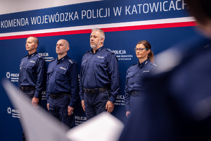 Grafika przedstawia trzech policjantów i policjantkę stojących na tle granatowego baneru z białym napisem komenda Wojewódzka Policji w Katowicach.