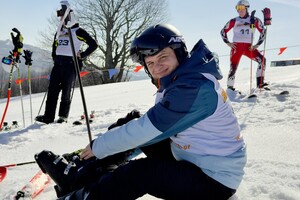 Zbliżenie na siedzącego na stoku zawodnika. Za nim dwaj stojący uczestnicy zawodów